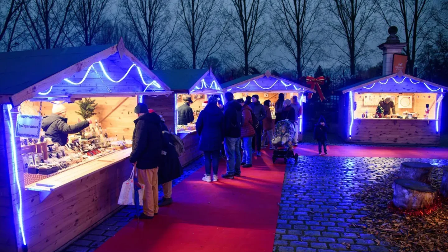 Chalets en bois illuminés sur la place Carnot à Lyon avec l’esplanade pavée et la façade de la gare de Perrache en arrière-plan